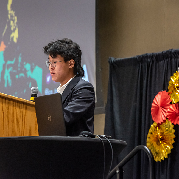 Student stands at the podium and speaks about his experiences at the AAPI kickoff event